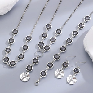 Detail of silver jewelry set with faceted black acrylic stones and hammered metal charms