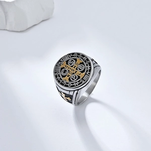 Detail shot of St. Benedict cross ring with silver and gold finish on white marble
