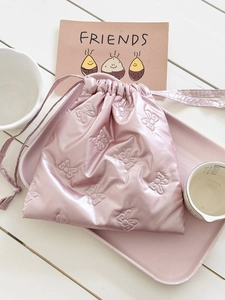 Detail of pink satin drawstring bag with embossed bow patterns in a lifestyle setting