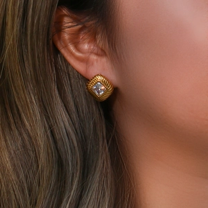 Close-up of a gold square zircon stud earring with textured metal edges on a model
