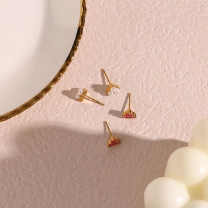 Detail of gold-plated stud earrings featuring red zircon and white pearls on pink texture