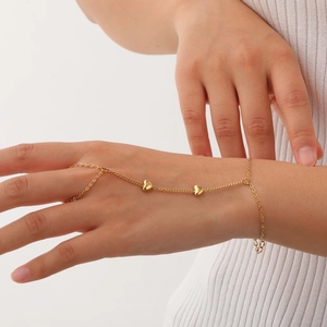 Detail of elegant gold-tone hand chain featuring delicate heart charms on woman's hand