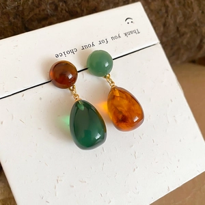 Macro detail of asymmetric resin water drop earrings with brown and green beads