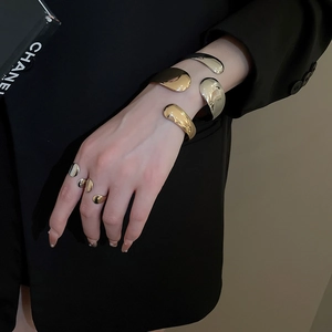 Detail of minimalist gold and silver liquid metal open bangles on a black sleeve