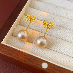 Detailed macro view of golden bow pearl earrings displayed in a beige velvet jewelry box