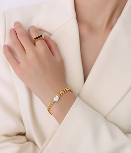 Golden wheat-link bracelet with heart pearl inlay and black ring worn on a model
