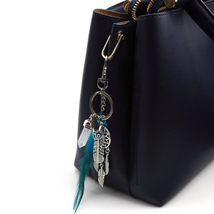 Detailed close-up of dreamcatcher keychain with teal feather on a blue leather bag