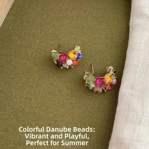 Macro shot of colorful beaded C-shaped earrings on textured dark green linen background