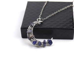 Close-up of crescent moon pendant with blue and grey crystals on a silver chain