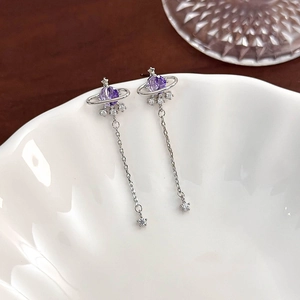 Detailed shot of silver planet tassel earrings with purple crystals on a ceramic bowl