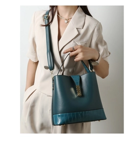 Detail of dark teal faux leather handbag with crocodile pattern texture and gold buckle