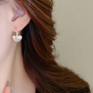Close-up of a silver heart-shaped earring with small diamonds on a female ear