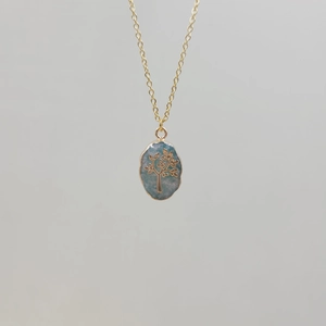 Detail of gold chain necklace featuring an oval light blue stone with tree of life motif