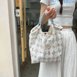 Close-up of quilted canvas bag with blue grid, bear patterns, and branding label