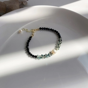 Detailed close-up of faceted black beads, teal crystals, and a pearl on a white ceramic dish
