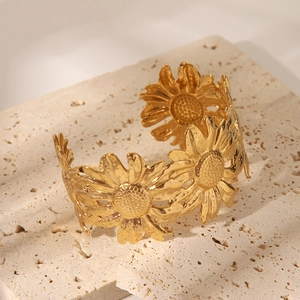Dettaglio del bracciale rigido a girasole dorato su sfondo in pietra naturale testurizzata
