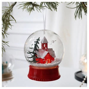 Christmas snow globe ornament with red cabin and snowy pine tree hanging on pine branch