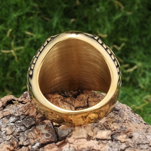Close-up of gold stainless steel ring with vintage cross engraving on rustic wood bark