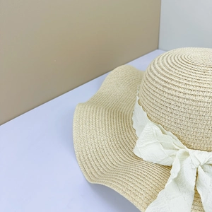Close-up of a woven straw hat with a white textured bow and natural wavy brim