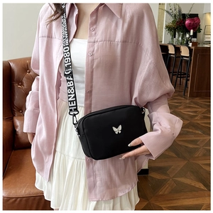Detail of black nylon crossbody bag featuring wide letter strap and silver butterfly ornament
