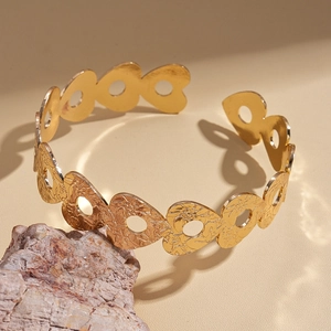 Dettaglio ravvicinato del bracciale dorato con cuori traforati e trame floreali a rilievo