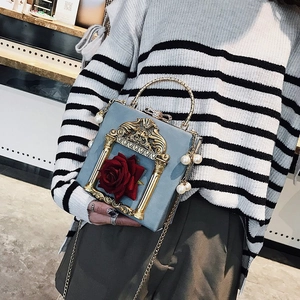Close-up of light blue vintage box bag featuring gold frame and red rose with pearl charm
