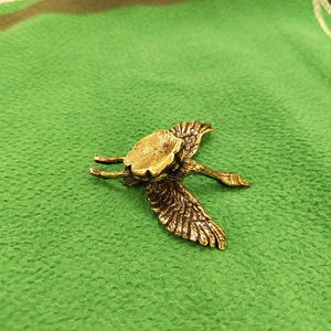 Brass crane bird figurine with feather texture on a green textured fabric background