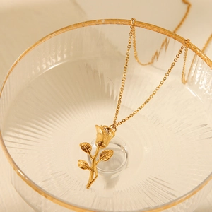 Detail shot of a golden rose pendant necklace inside a decorative glass bowl