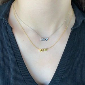 Close-up of gold and silver necklaces featuring M letter and heart pendants on a model