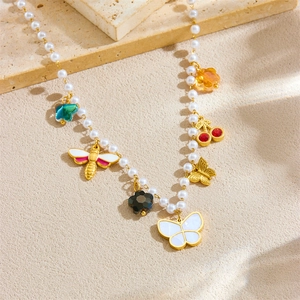 Gold pearl necklace with bee, butterfly, cherry, and flower charms on stone background