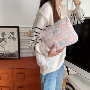 Detailed plush rainbow striped cosmetic bag held by a model in a cozy indoor setting