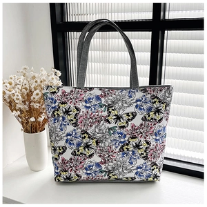 Detail of floral canvas tote bag featuring vibrant butterfly patterns and sturdy grey handles