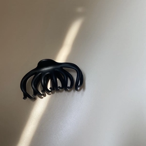 Detailed macro view of a large black claw clip with multi-claw design on a beige surface