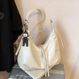 Retro white PU leather crescent shoulder bag with plush charm on a silver suitcase