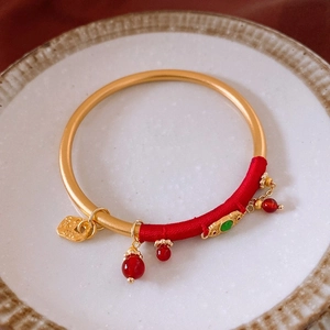 Détail d'un bracelet doré vintage avec fil de soie rouge et pendentif porte-bonheur