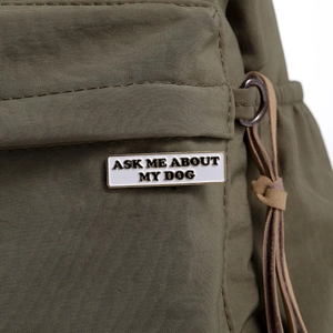 Detail shot of 'ASK ME ABOUT MY DOG' enamel pin on a dark green canvas fabric bag