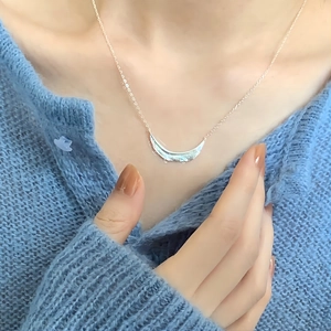 Close-up of 925 silver leaf texture necklace worn on a blue knitted sweater background