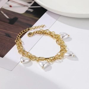 Detail of golden double-chain bracelet featuring white heart-shaped pearl charms and clasp