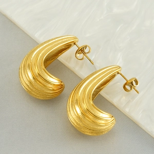 Detailed close-up of chunky gold ribbed C-shape earrings on a white marble background