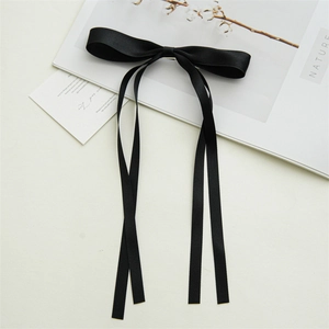 Detail shot of a black satin bow hair clip with long ribbons on a white background