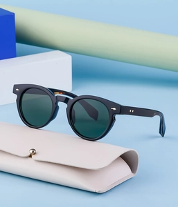 Detail of black oval sunglasses with gold diamond rivets and a beige leather case