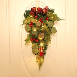 Close-up of Christmas swag with red plaid bow, berries, and LED lights on white door