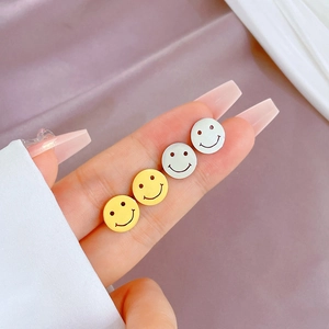 Minimalist circular smiley face stud earrings in gold and silver finish shown on fingertip