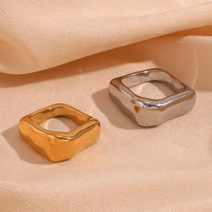 Gros plan de bagues carrées ondulées or et argent sur un fond de tissu en soie beige