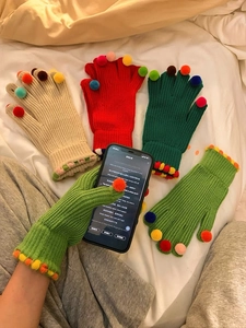 Dettaglio di pompon colorati su guanti in maglia con funzione touch screen per cellulari