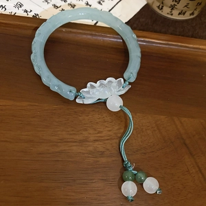 Gros plan d'un bracelet en jade avec pendentif lotus sur plateau en bois