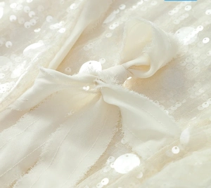 Detail shot of white sequins and a delicate ribbon bow on the sleeve of this elegant shirt