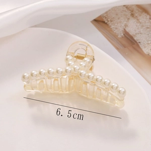 Close-up of 6.5cm transparent hair claw clip with white pearls on a ceramic plate
