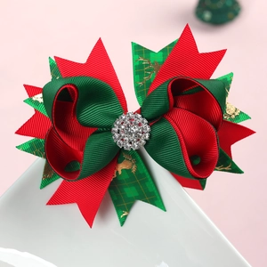 Macro detail of Christmas bow hair clip with gold reindeer pattern and rhinestone center