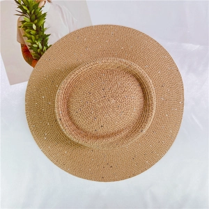 Detailed overhead view of woven straw sun hat with silver sequins on white silk fabric